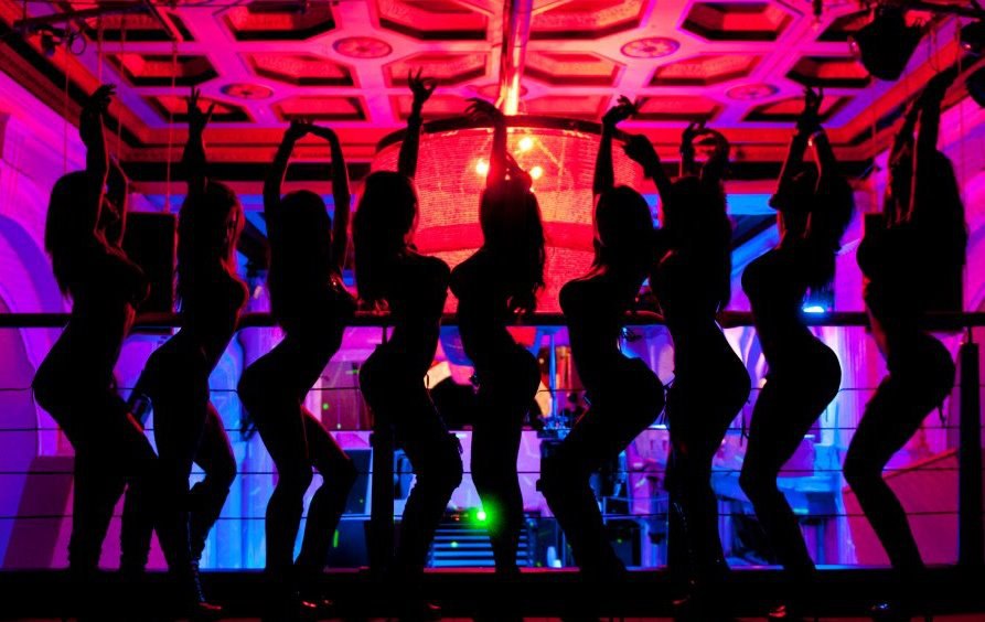 Телочка в парике танцует стриптиз для группы посетителей в клубе